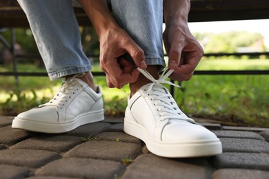 Photo of Man tying shoelace of white sneaker outdoors, closeup