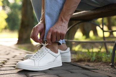 Photo of Man tying shoelace of white sneaker outdoors, closeup