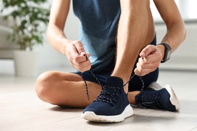 Man tying shoelace of sneaker indoors, closeup