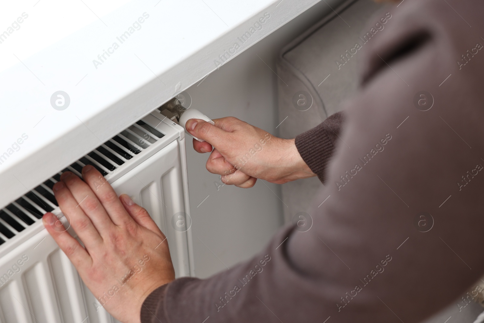 Photo of Man adjusting temperature of heating radiator indoors, closeup