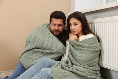 Photo of Couple with blanket warming up near heating radiator at home