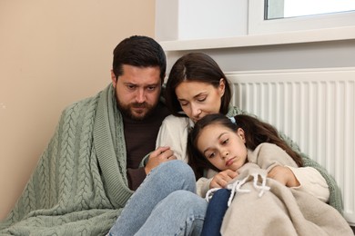 Photo of Family with blankets warming near heating radiator at home