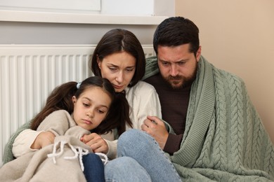 Photo of Family with blankets warming near heating radiator at home