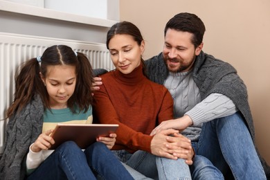 Photo of Happy family with tablet warming near heating radiator at home