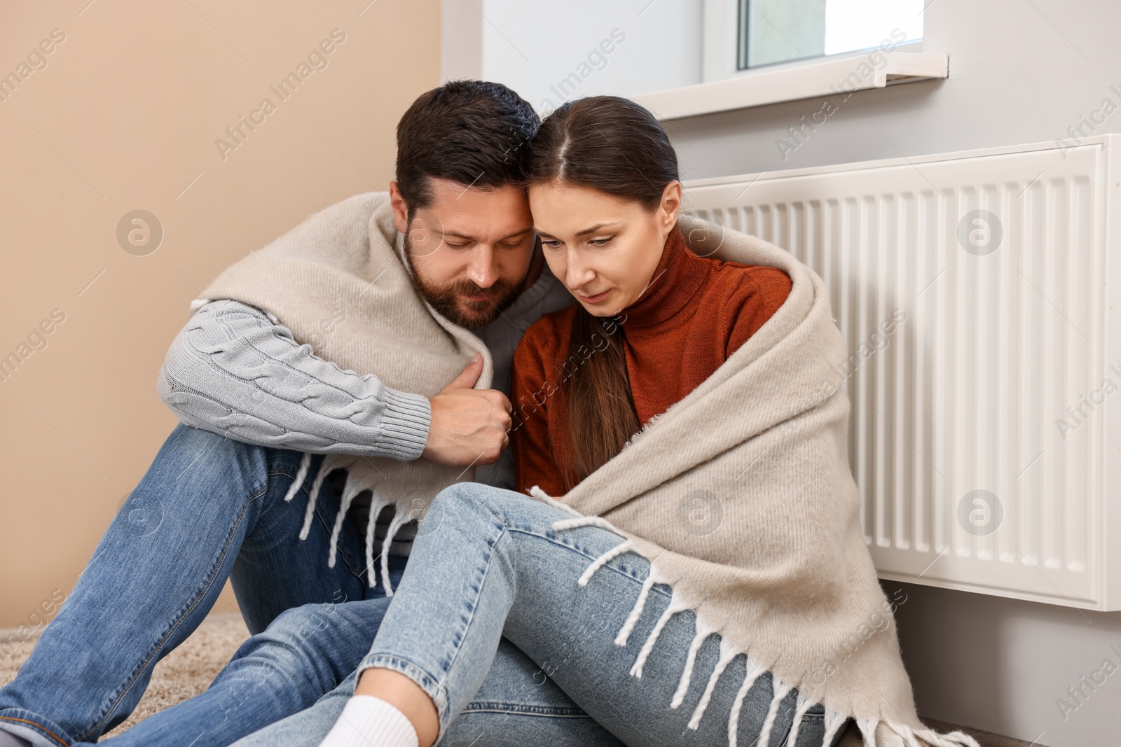 Photo of Couple with blanket warming up near heating radiator at home