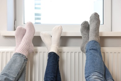 Photo of Family warming feet near heating radiator at home, closeup