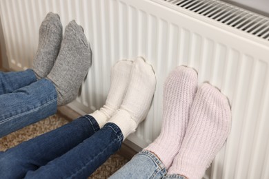 Family warming feet near heating radiator at home, closeup