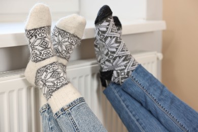 Photo of Couple warming feet near heating radiator at home, closeup