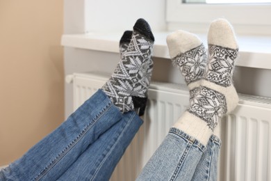 Couple warming feet near heating radiator at home, closeup