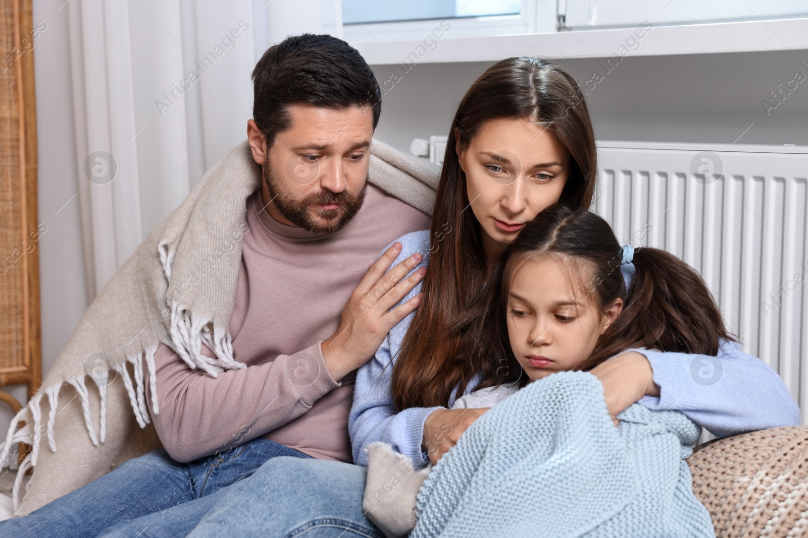 Photo of Family with blankets warming near heating radiator at home