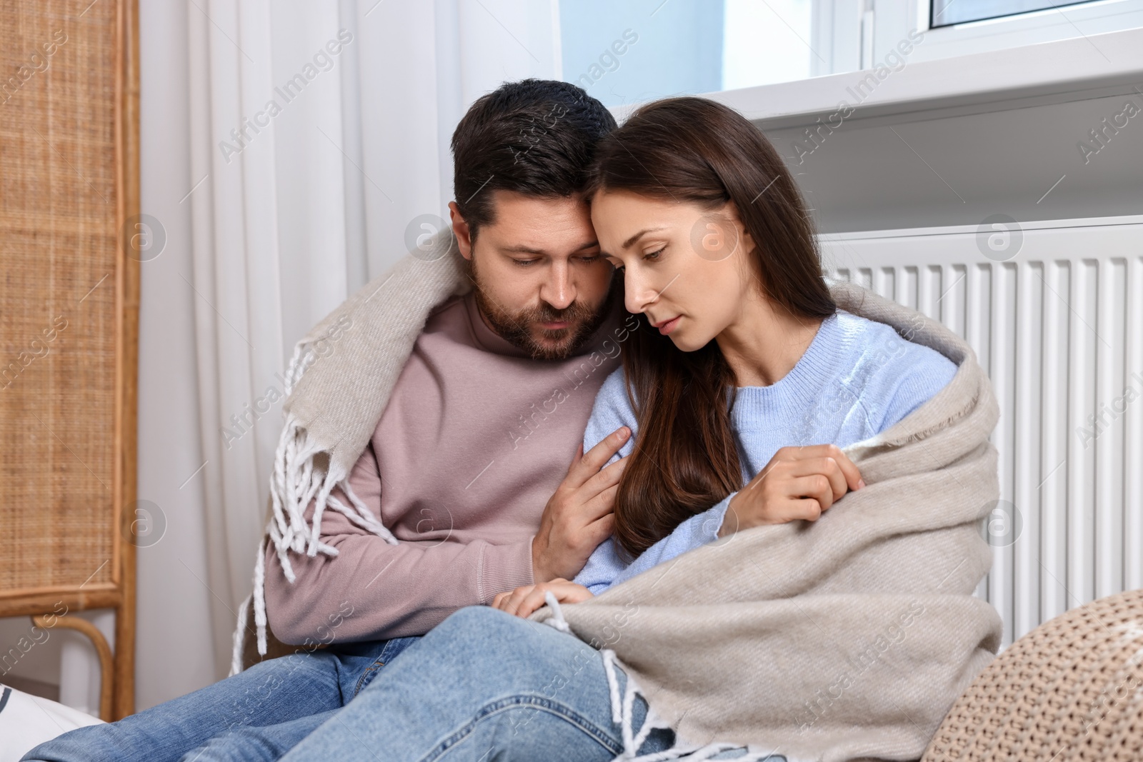 Photo of Couple with blanket warming up near heating radiator at home