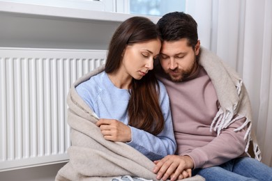Photo of Couple with blanket warming up near heating radiator at home