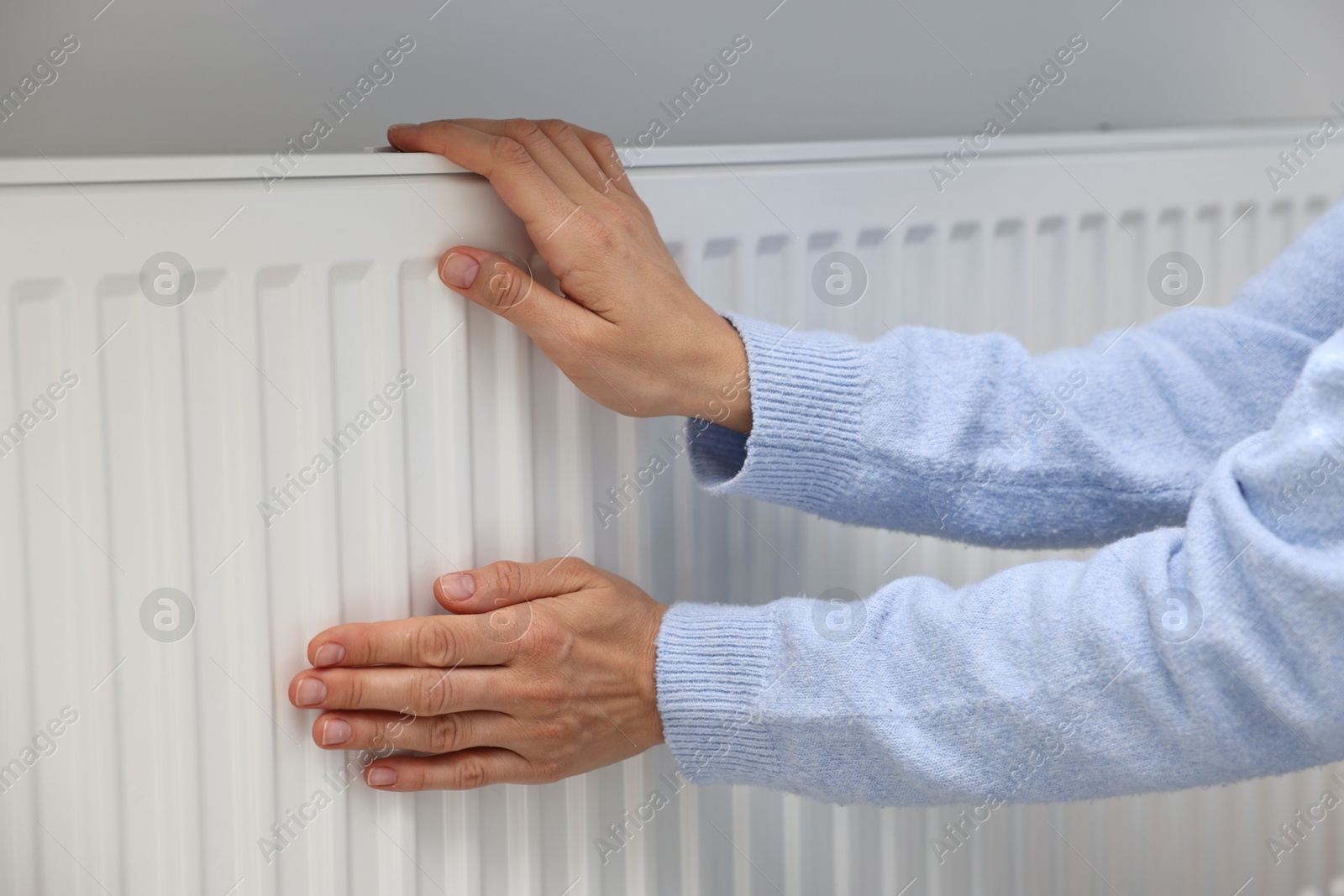 Photo of Woman warming hands near heating radiator indoors, closeup