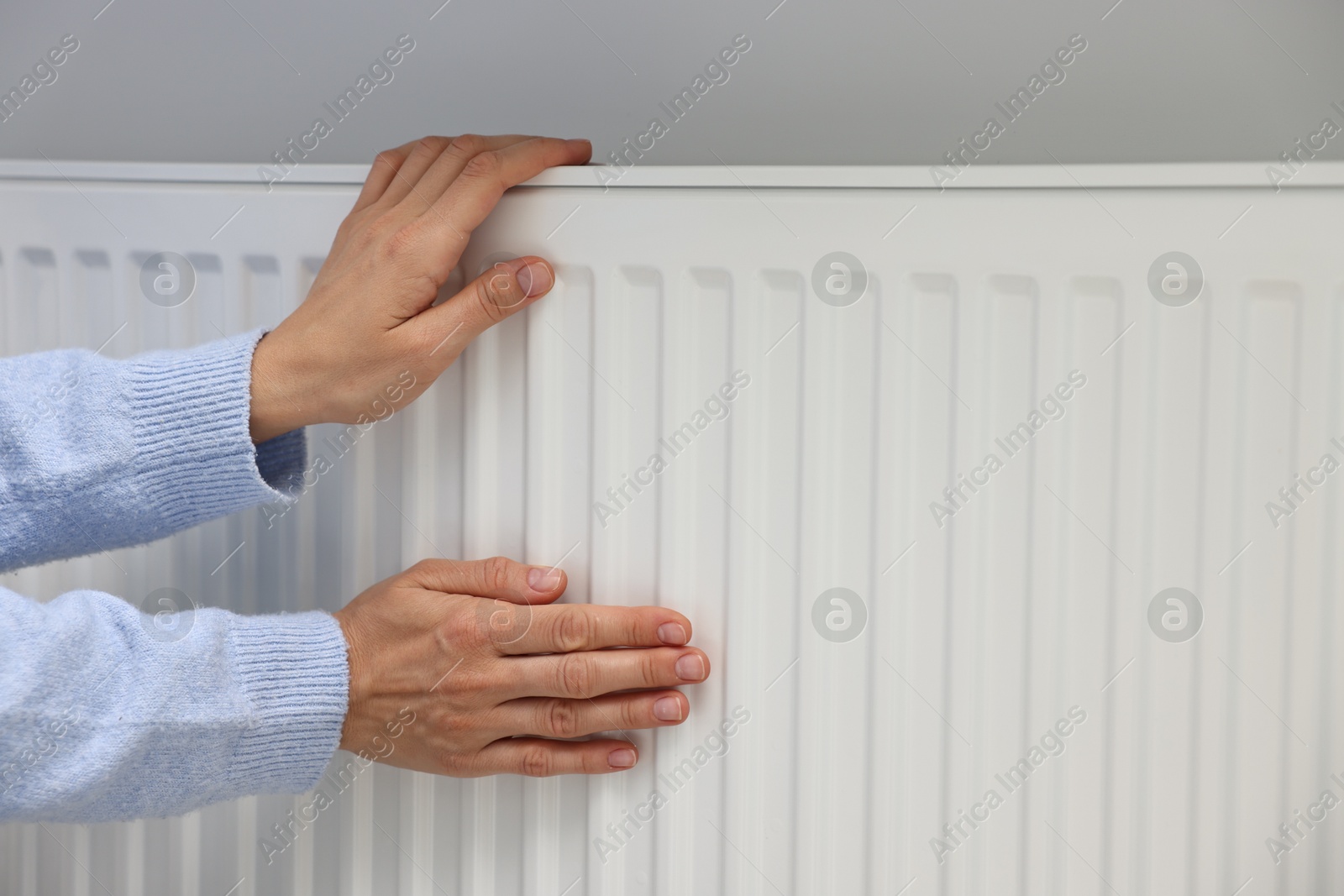 Photo of Woman warming hands near heating radiator indoors, closeup