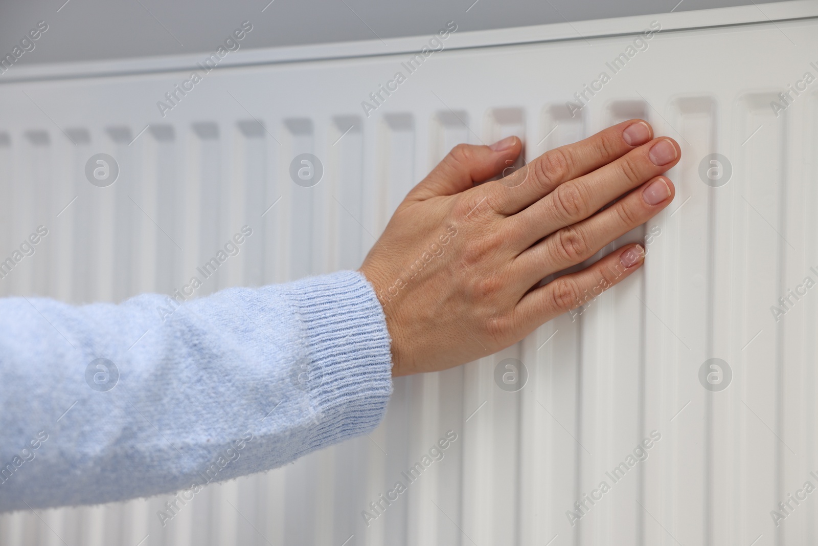 Photo of Woman warming hand near heating radiator indoors, closeup