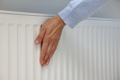 Photo of Woman warming hand near heating radiator indoors, closeup