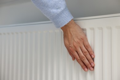 Woman warming hand near heating radiator indoors, closeup