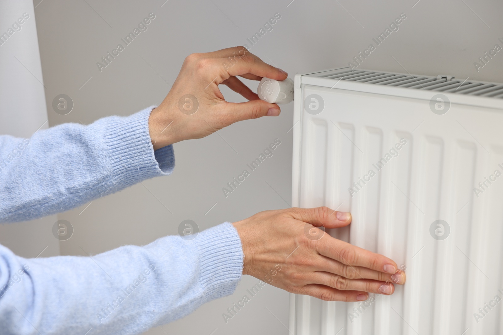 Photo of Woman adjusting temperature of heating radiator indoors, closeup