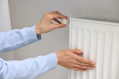 Photo of Woman adjusting temperature of heating radiator indoors, closeup