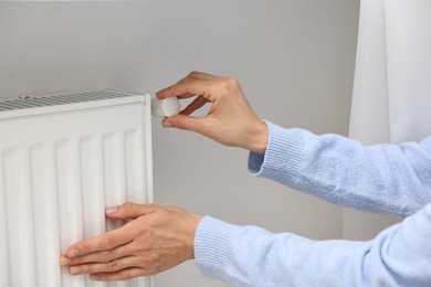 Photo of Woman adjusting temperature of heating radiator indoors, closeup