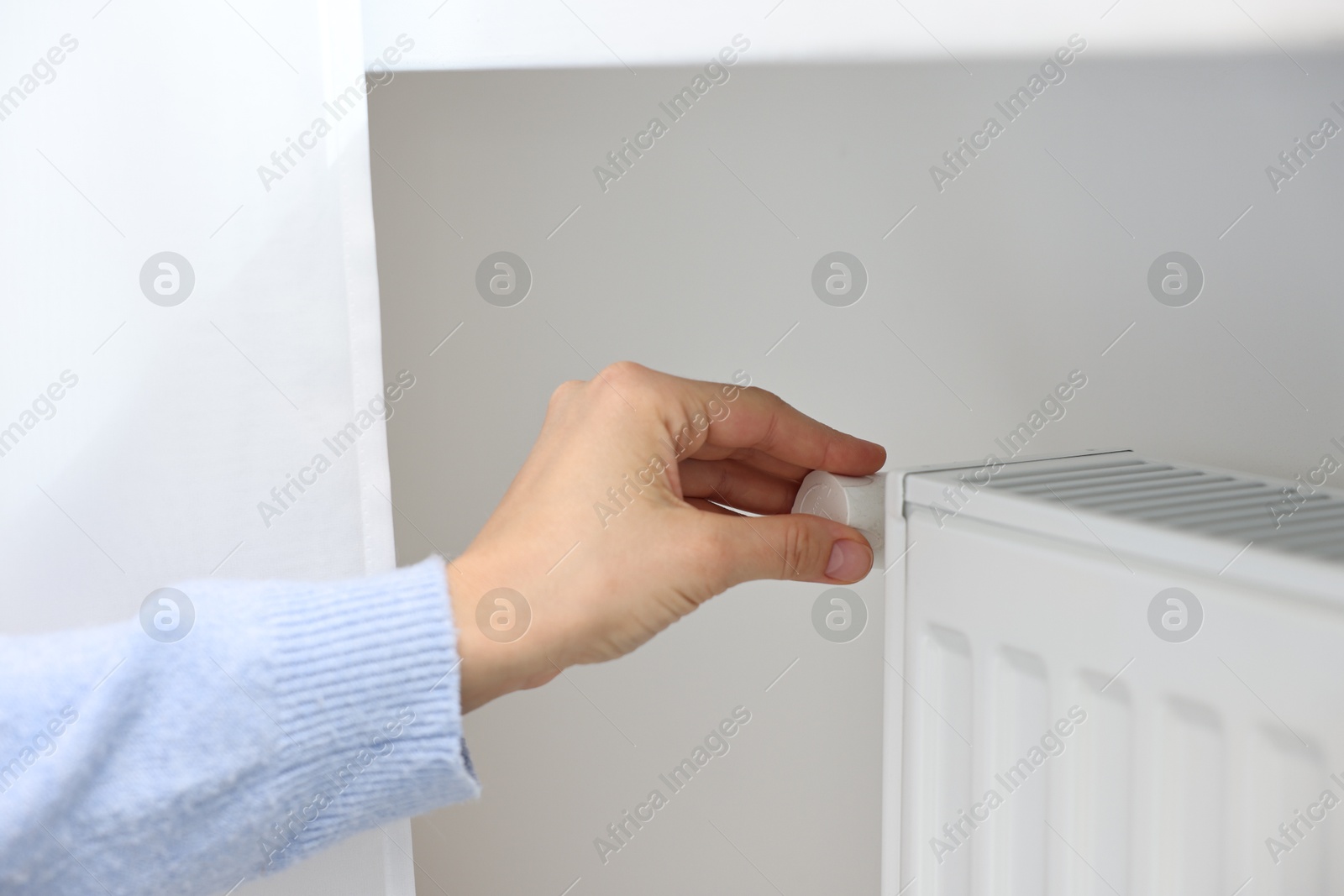 Photo of Woman adjusting temperature of heating radiator indoors, closeup