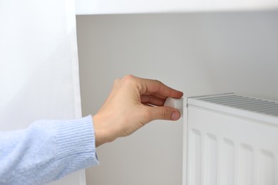 Photo of Woman adjusting temperature of heating radiator indoors, closeup