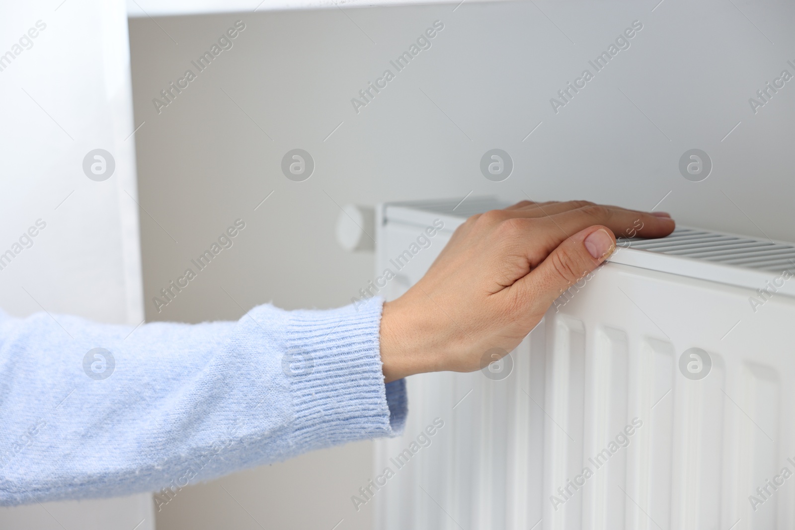 Photo of Woman warming hand near heating radiator indoors, closeup