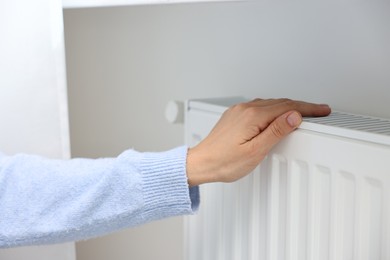 Woman warming hand near heating radiator indoors, closeup