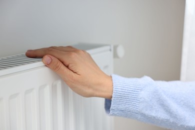 Photo of Woman warming hand near heating radiator indoors, closeup