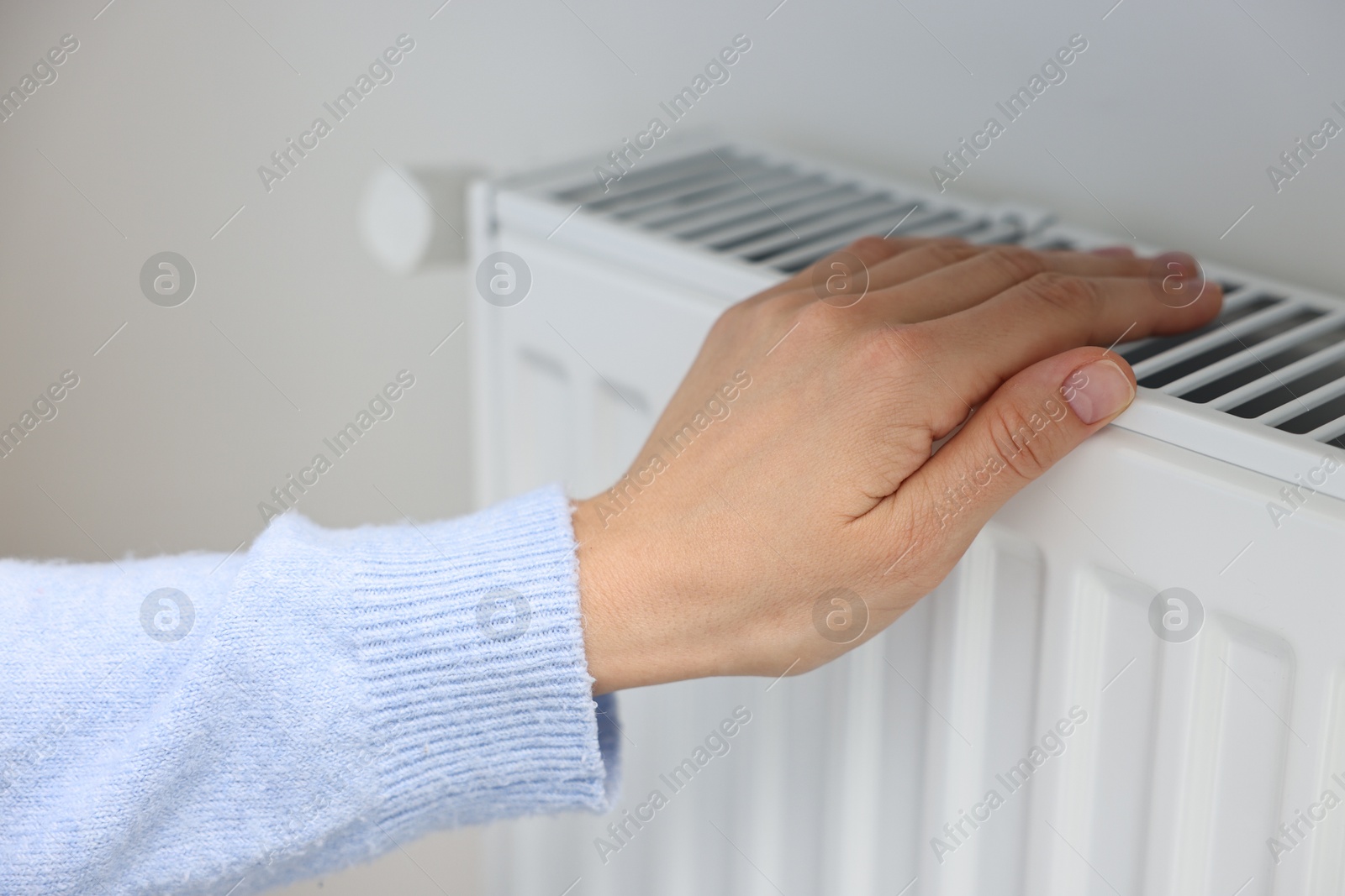 Photo of Woman warming hand near heating radiator indoors, closeup