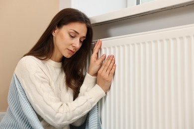 Photo of Woman with blanket warming near heating radiator at home