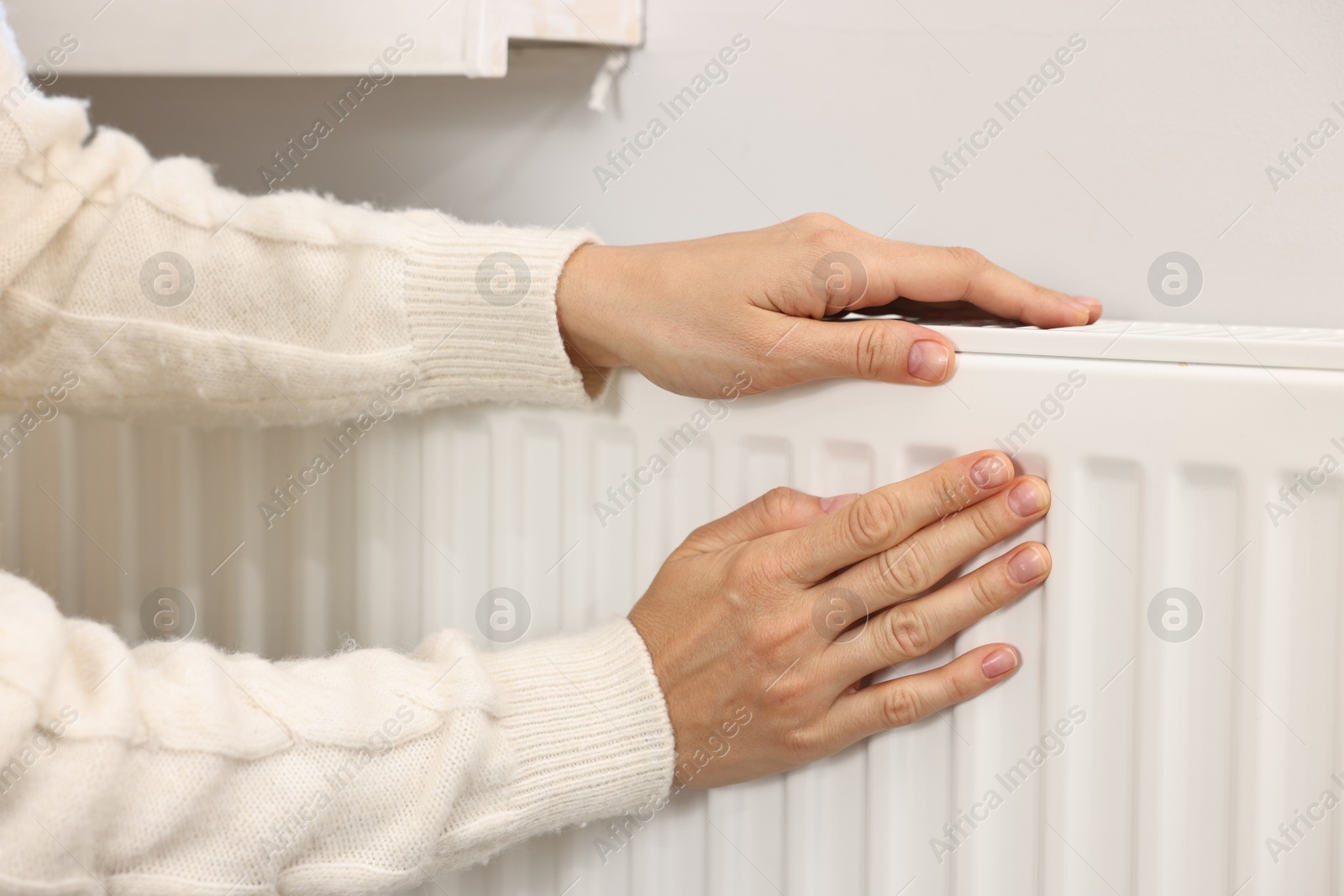 Photo of Woman warming hands near heating radiator at home, closeup