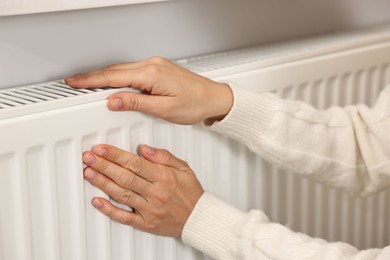 Woman warming hands near heating radiator at home, closeup