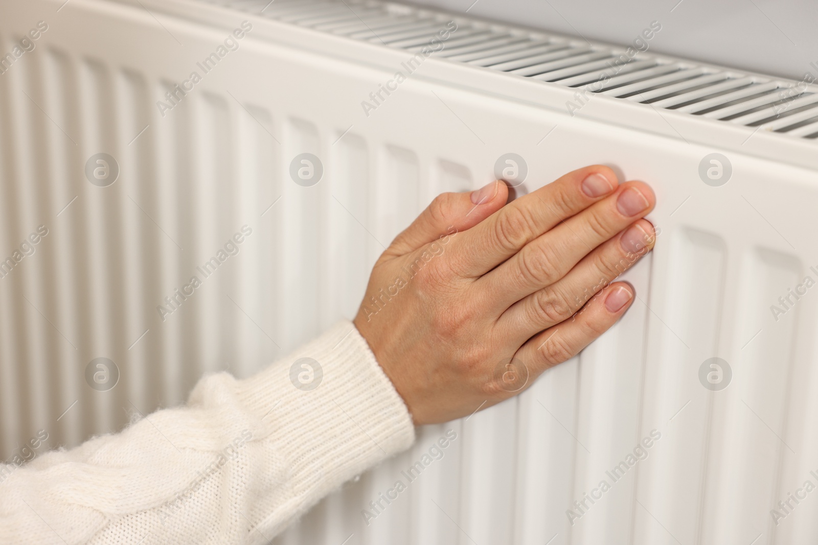 Photo of Woman warming hand near heating radiator at home, closeup