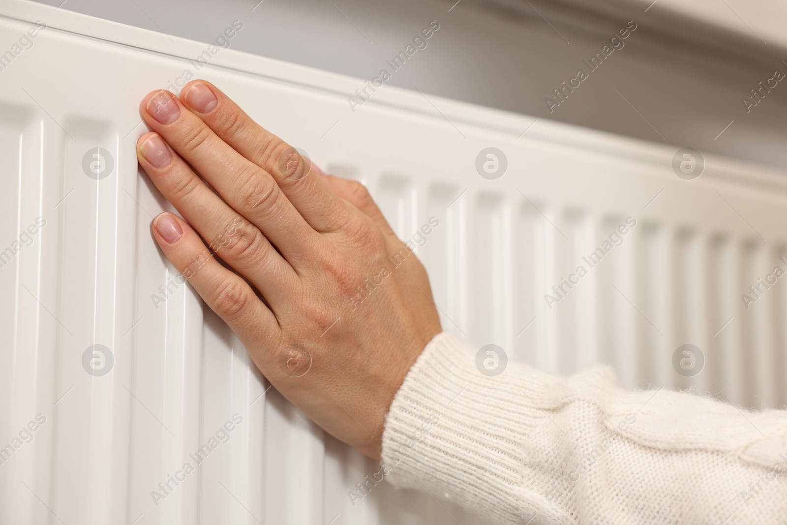 Photo of Woman warming hand near heating radiator at home, closeup