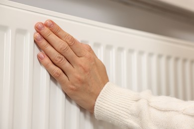 Photo of Woman warming hand near heating radiator at home, closeup