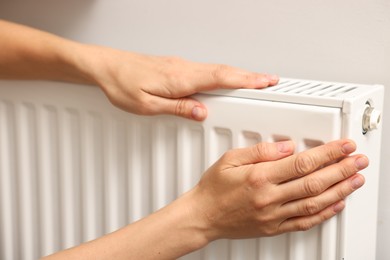 Woman warming hands near heating radiator indoors, closeup