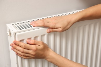 Woman warming hands near heating radiator indoors, closeup