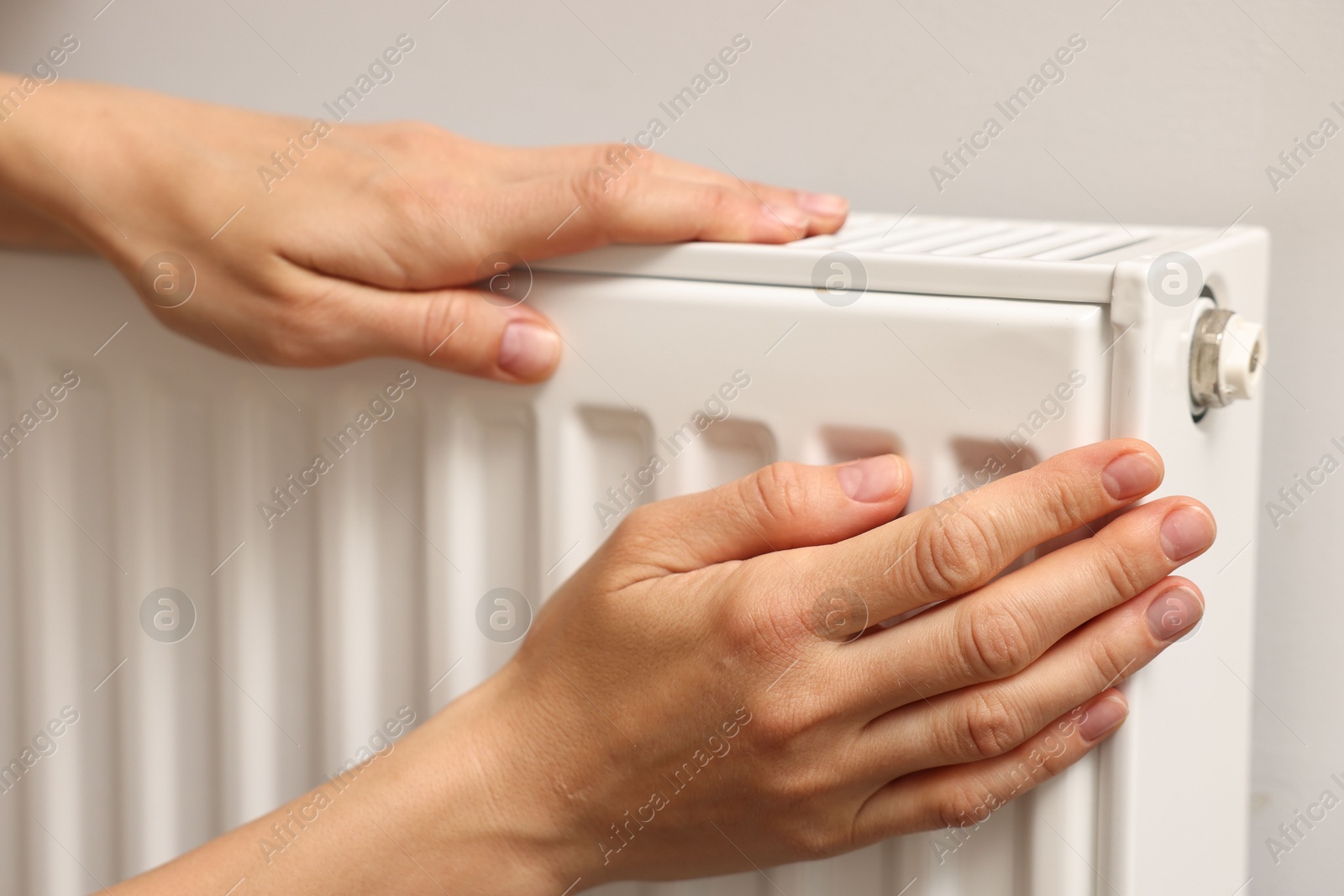 Photo of Woman warming hands near heating radiator indoors, closeup