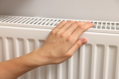 Woman warming hand near heating radiator indoors, closeup