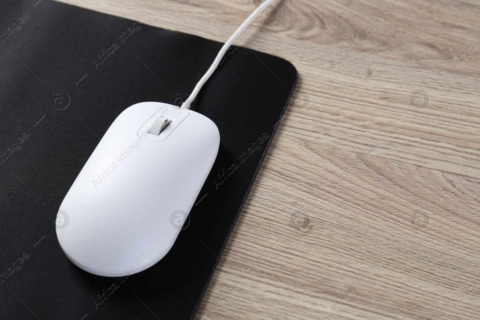 Photo of White computer mouse and black mousepad on wooden table, closeup