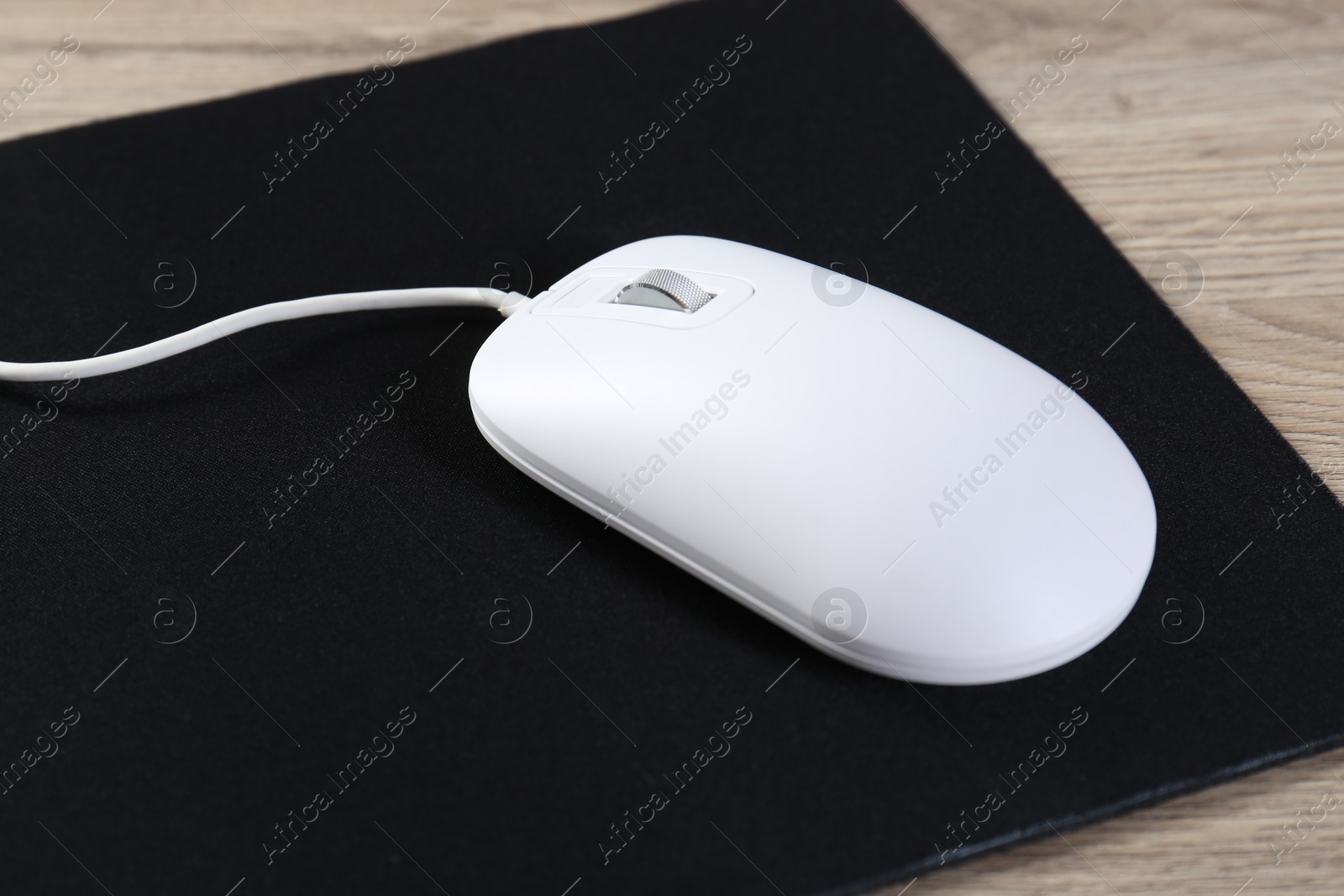 Photo of White computer mouse and black mousepad on wooden table, closeup