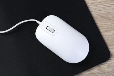 Photo of White computer mouse and black mousepad on wooden table, top view