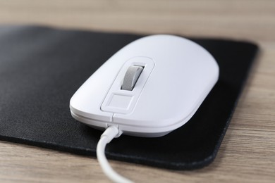 Photo of White computer mouse and black mousepad on wooden table, closeup