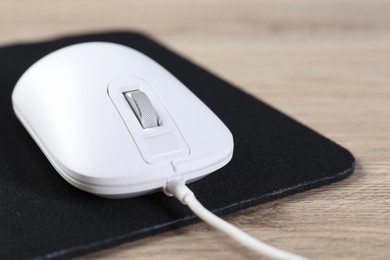 Photo of White computer mouse and black mousepad on wooden table, closeup