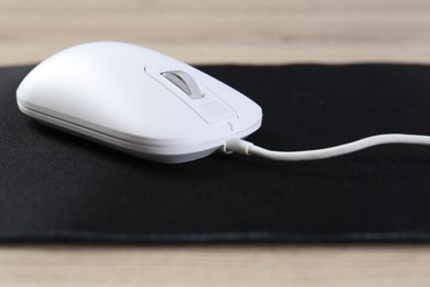 Photo of White computer mouse and black mousepad on wooden table, closeup