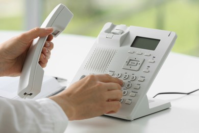 Photo of Assistant dialing number on telephone against blurred background, closeup