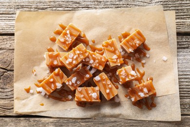 Photo of Yummy candies with caramel sauce and sea salt on wooden table, top view