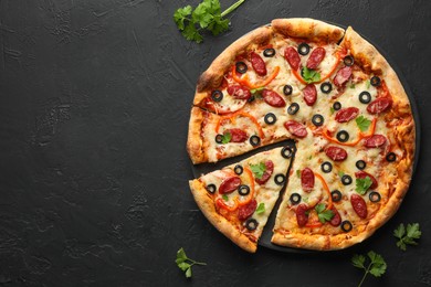 Photo of Tasty pizza with dry smoked sausages, olives, pepper and parsley on black table, top view. Space for text