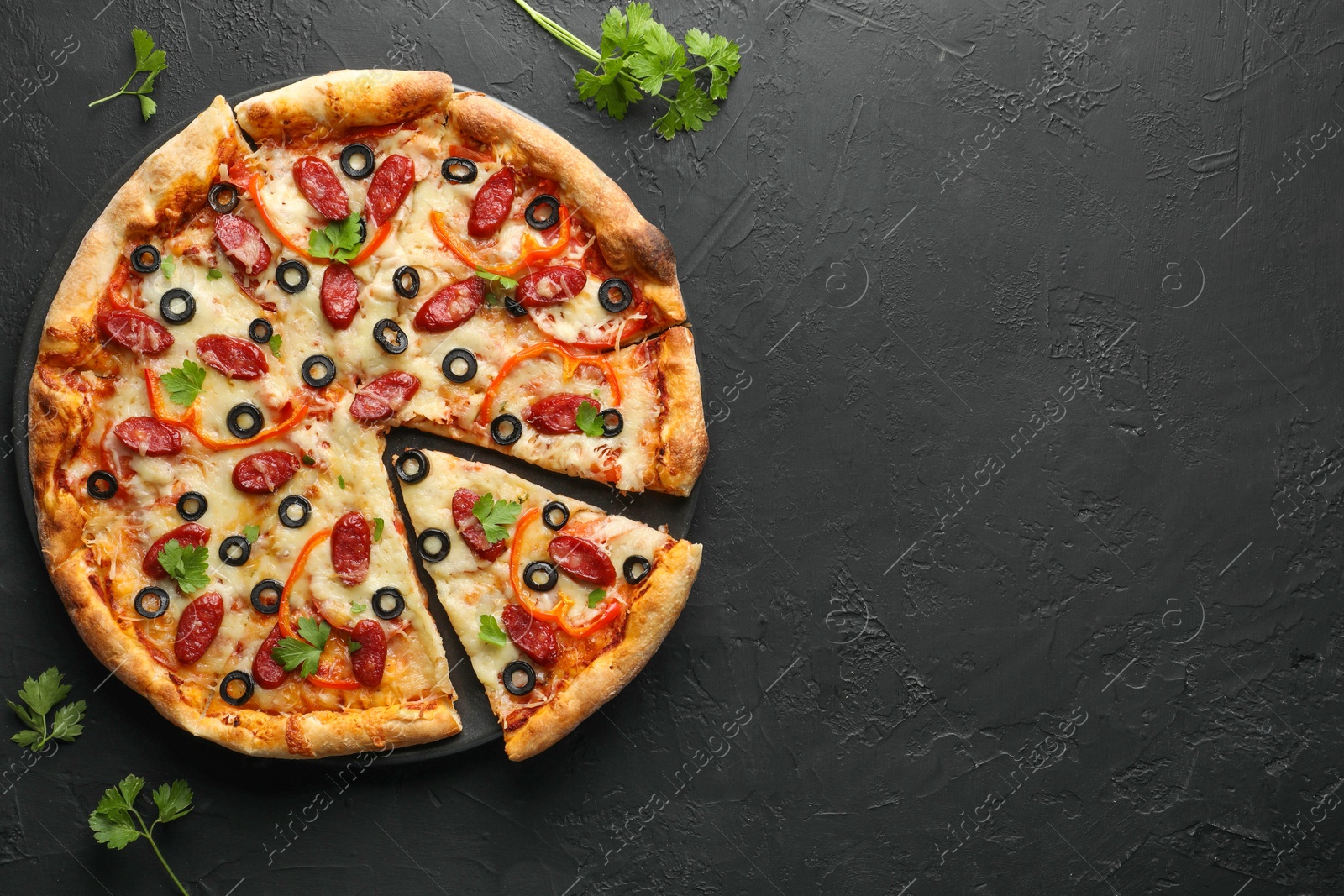 Photo of Tasty pizza with dry smoked sausages, olives, pepper and parsley on black table, top view. Space for text